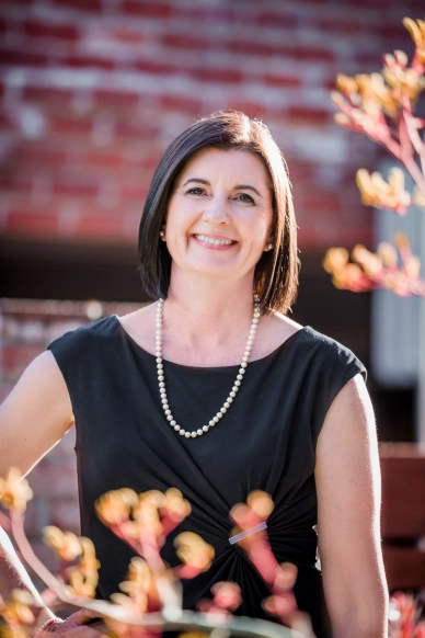 Photograph of Ariadne Horstman, smiling, looking straight ahead, wearing a black shirt and a strand of pearls