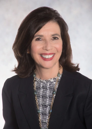 Photograph of Donna Rasile, smiling and looking directly forward, wearing a black blazer and patterned gray colored shirt