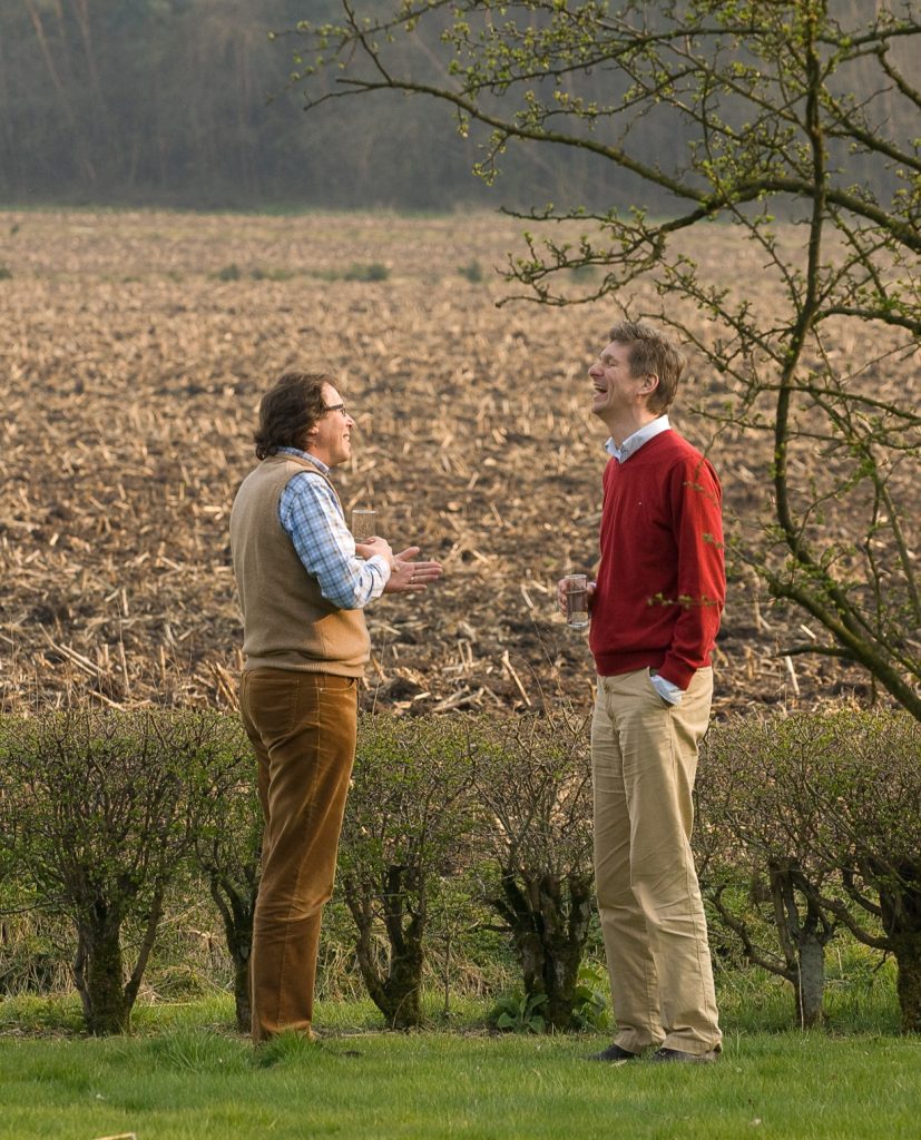 Two colleagues laughing in front of a corn field and hedge row.