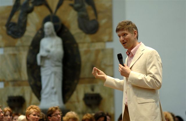 Man in a white blazer speaking to an audience.