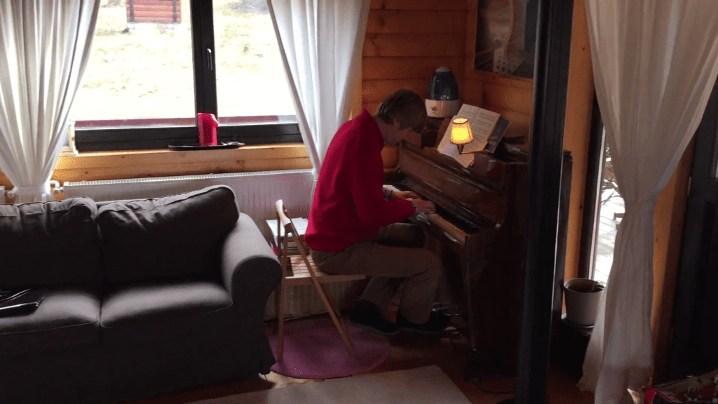 Man in a red shirt playing the piano in a living room.