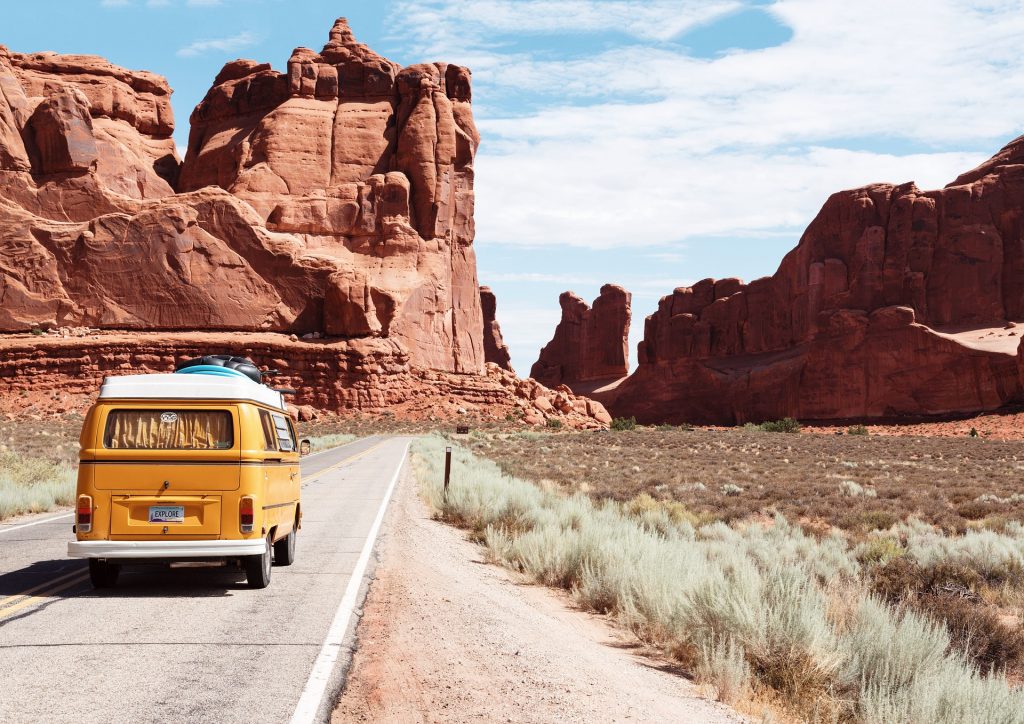 yellow camper van on a paved road entering arches national park